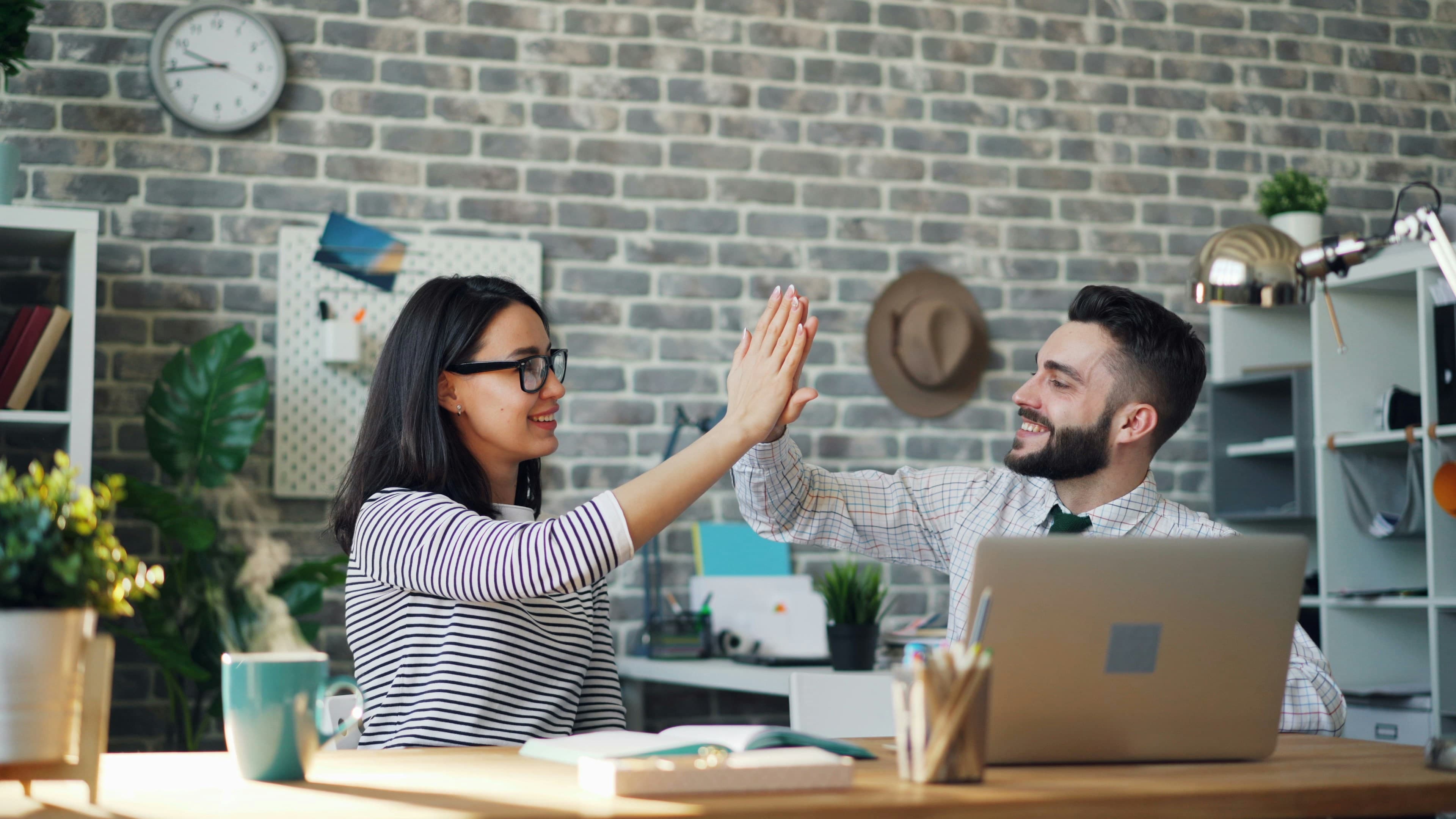 Young man and woman giving high five over laptop